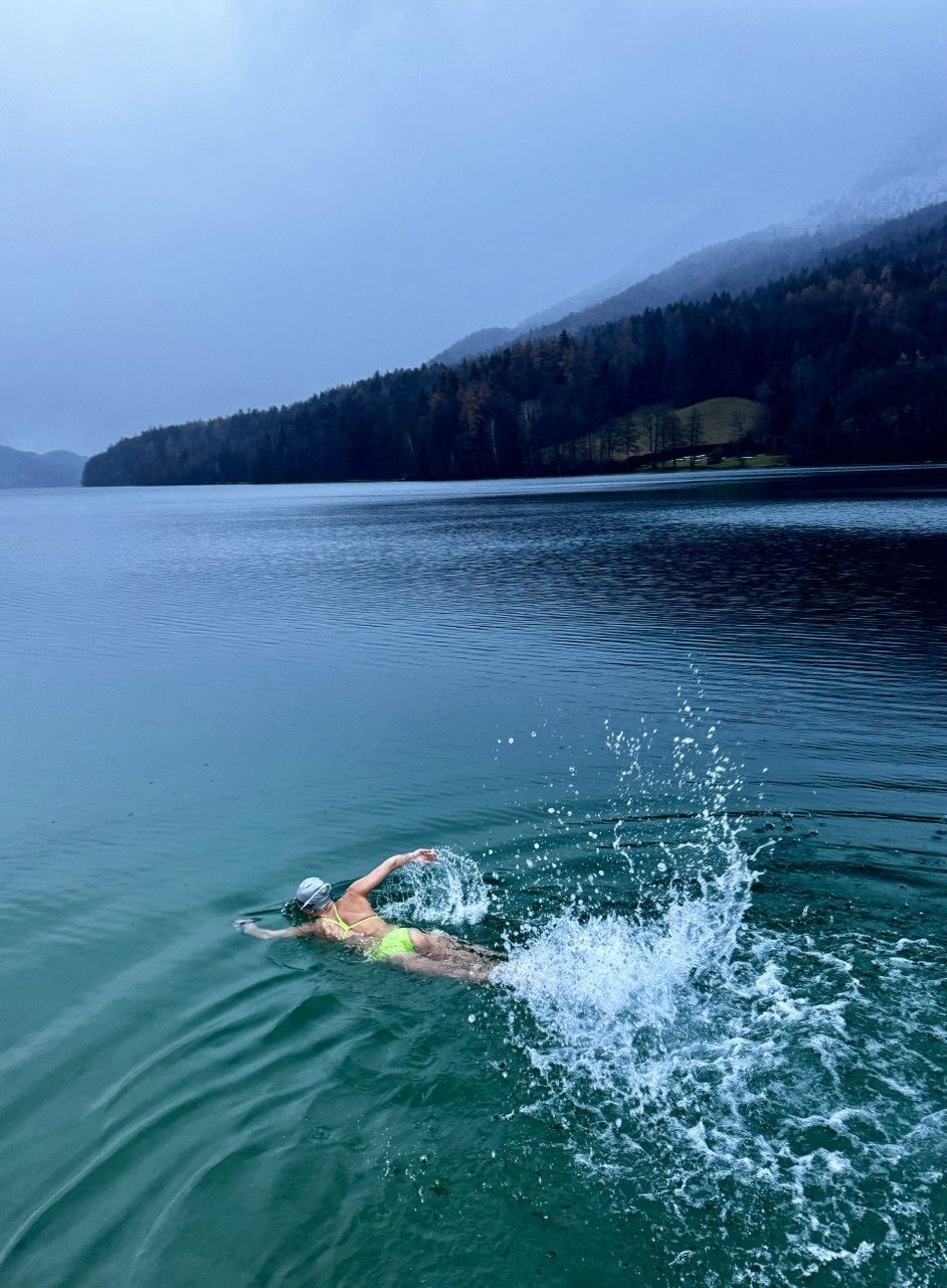 Ines Hahn krault in einem kalten Bergsee, im Hintergrund bewaldete Berghänge im Nebel